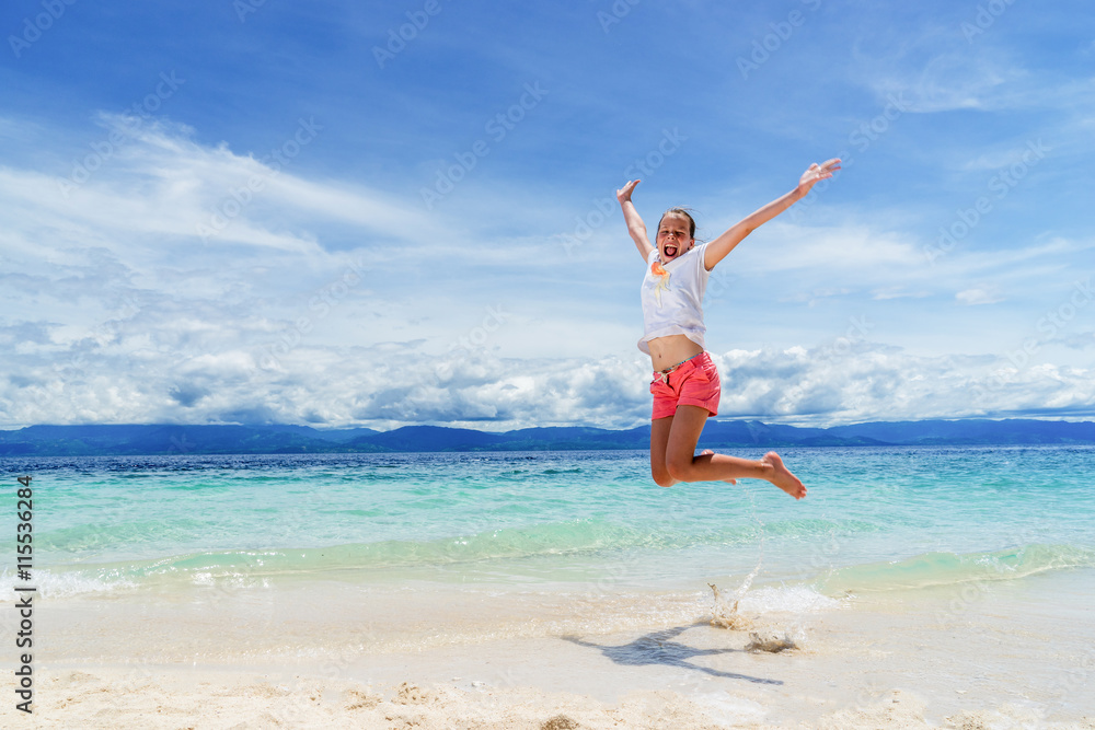 young girl is juming on the beach with white sand and blue sky