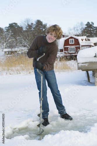 Sweden, Stockholm County, Dalaro, Portrait of teenager making hole for ice fishing photo