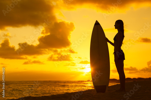 Female surfer holding surfboard against a beautiful sunset. 