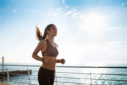 Fototapeta Naklejka Na Ścianę i Meble -  Picture of young attractive fitness girl jogging with sea on background