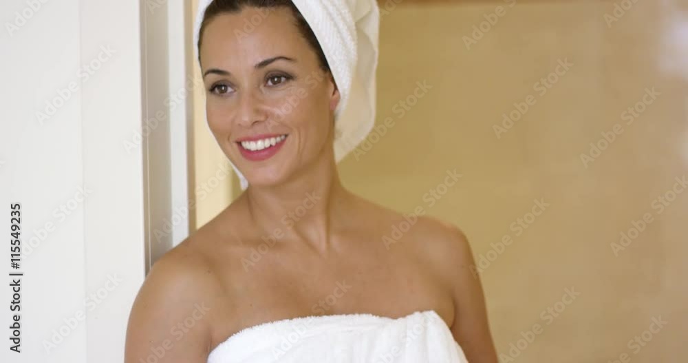 Woman wearing towel and with hair wrapped smiles over shoulder while standing in door frame Woman wearing towel and with hair wrapped smiles over shoulder while standing in door frame