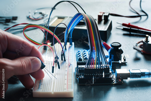 Circuits creation with electronic components. Closeup on programmer hand connecting led with breadboard and microcontroller. Programming, electronics development, innovation in technologies photo