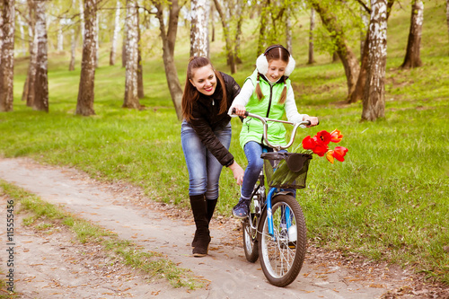 happy mother teaches his daughter to ride a bike in the park