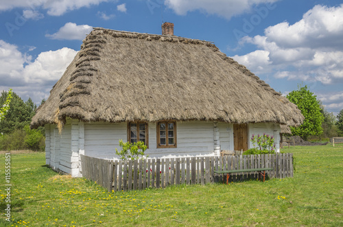 wiejski mały, biały domek pokryty strzechą z ogródkiem