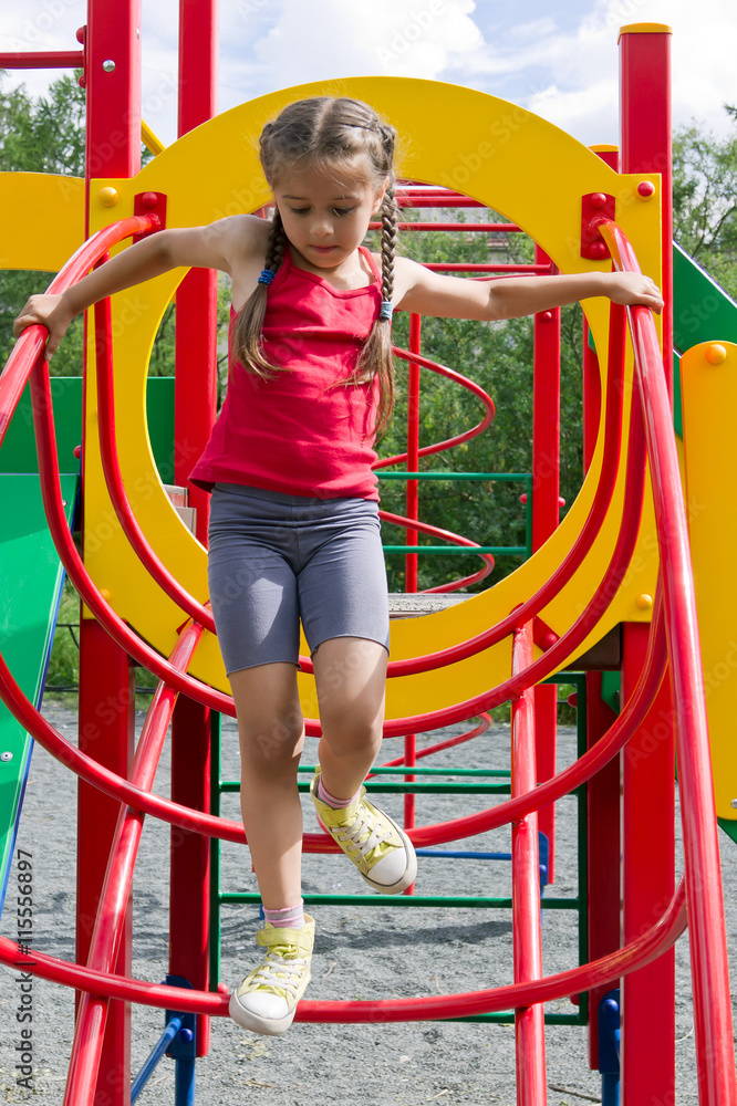 Little caucasian girl dressed in a red jersey playing on playground, coming down the stairs Little caucasian girl dressed in a red jersey playing on playground, coming down the stairs