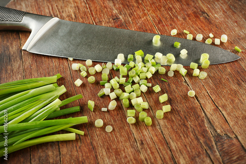 Fresh green onion with knife on cutting board, closeup