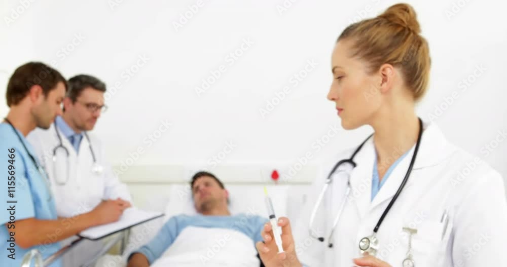 Doctors speaking with sick patient in bed while nurse prepares needle Doctors speaking with sick patient in bed while nurse prepares needle
