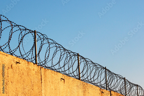 Barbed wire on concrete fence against blue sky background