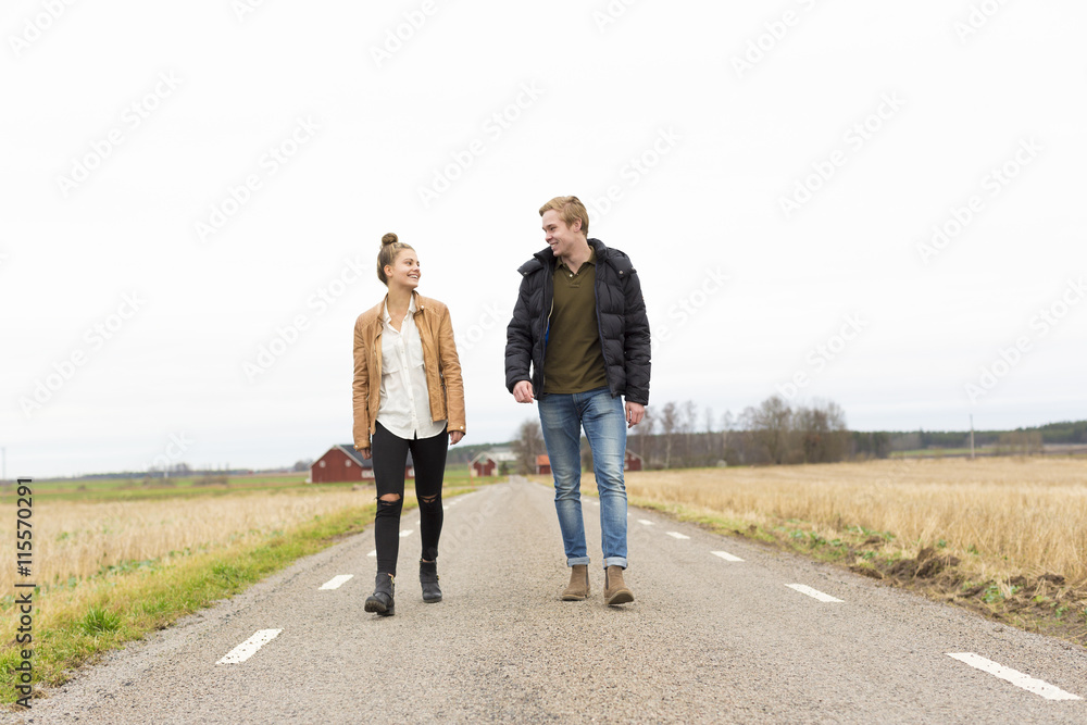 Sweden, Ostergotland, Mjolby, Teenage girl (14-15) and young man walking along country road Sweden, Ostergotland, Mjolby, Teenage girl (14-15) and young man walking along country road