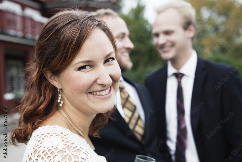 Sweden, Smaland, Bride looking at camera with groom and best man in background Sweden, Smaland, Bride looking at camera with groom and best man in background