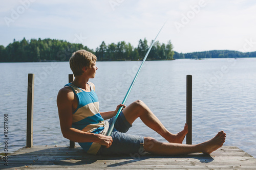 Young man fishing in lake while sitting on pier  photo