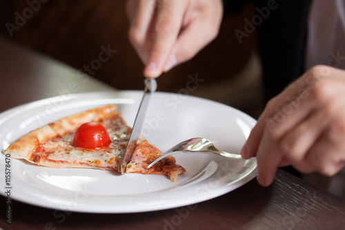 Man at home eating a slice of pizza and social networking with a