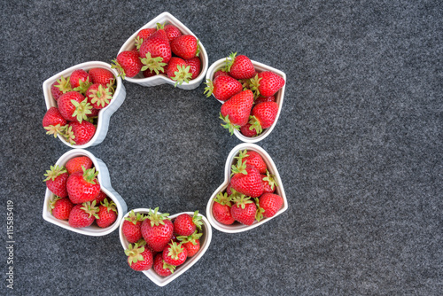 Fresh picked strawberries in white heart shaped bowls, on a gray background 