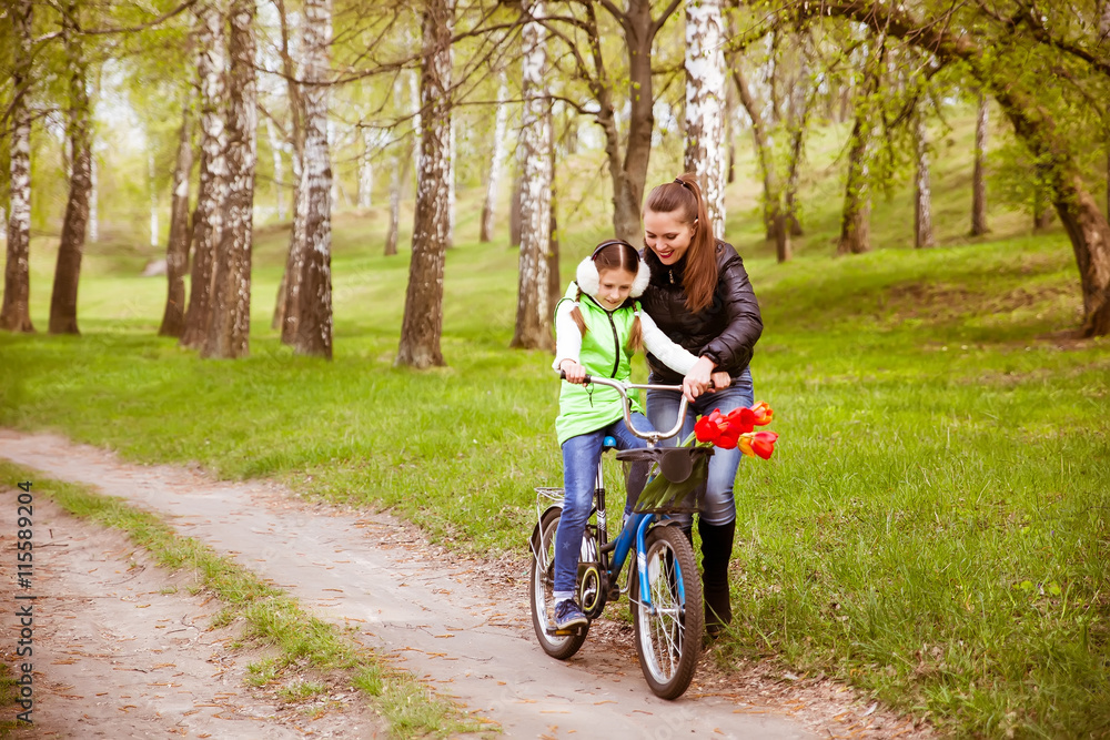 happy mother teaches his daughter to ride a bike. Mother holds daughter from falling