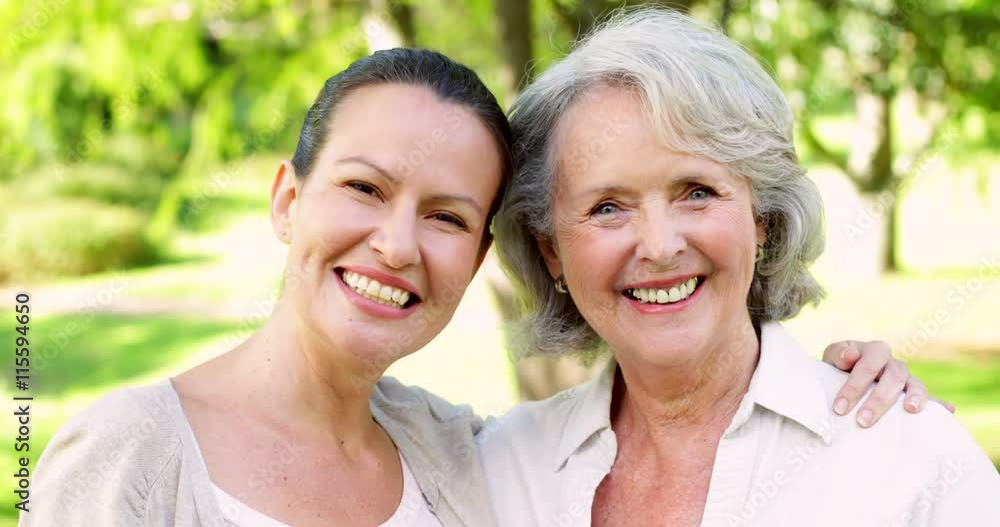Mother and adult daughter smiling at camera in the park Mother and adult daughter smiling at camera in the park