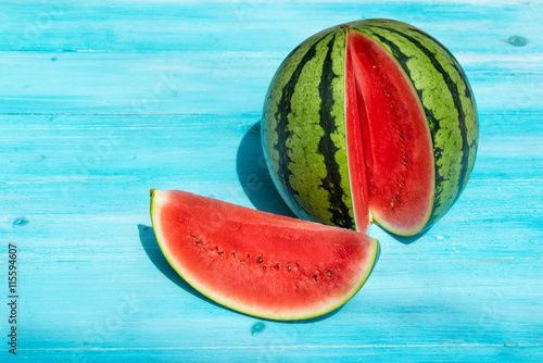 Fresh watermelon with one section sliced on blue wooden background