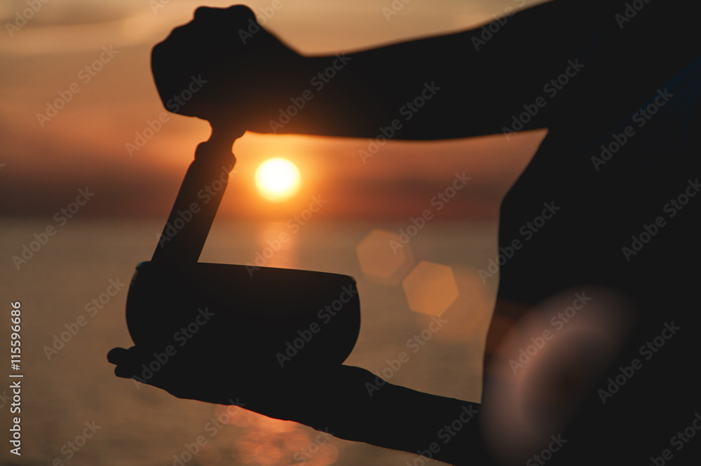 Practice with singing bowl at the beach at sunset. Lens flare effect