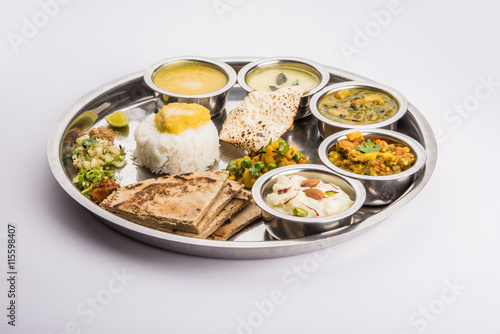 typical maharashtrian food served in a steal plate, marathi food includes kadhi and shrikhand, plain dal, spinach curry, aalu mutter, plain rice, papad, bhakri or bhakar or roti and variety of salad