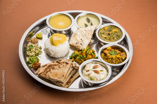 typical maharashtrian food served in a steal plate, marathi food includes kadhi and shrikhand, plain dal, spinach curry, aalu mutter, plain rice, papad, bhakri or bhakar or roti and variety of salad photo