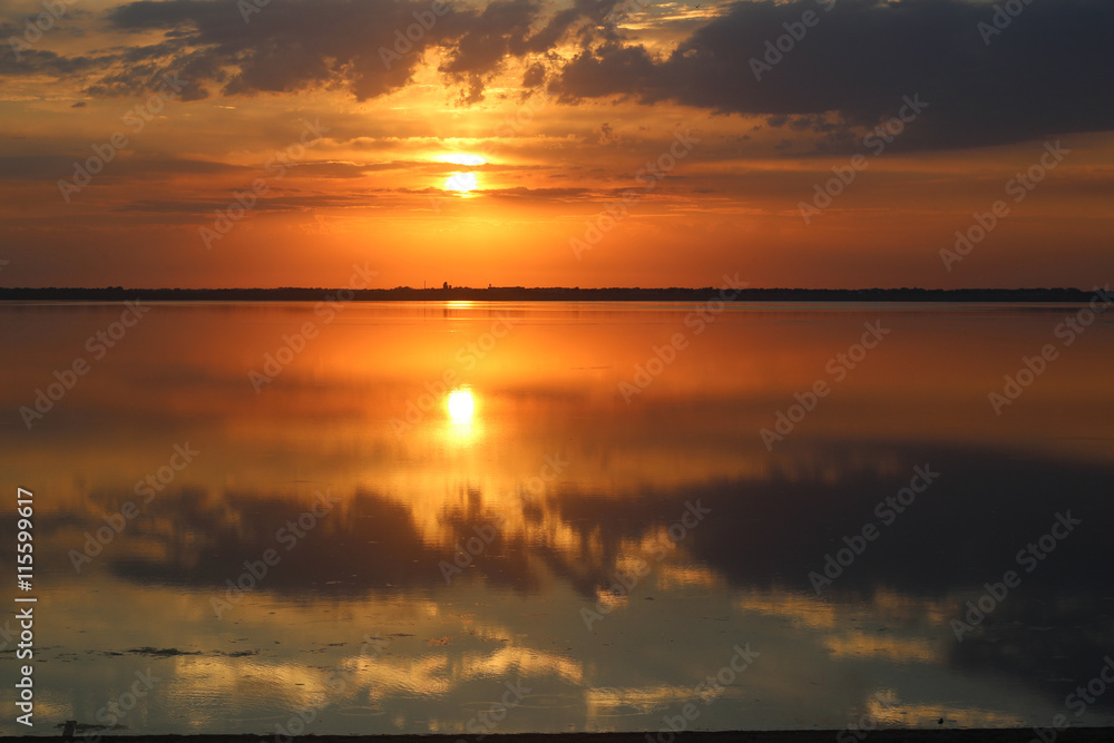 Beautiful colourful orange sunset over a calm lake. Reflection of clouds in water