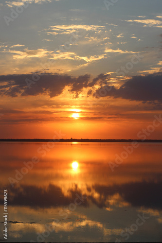 Beautiful colourful orange sunset over a calm lake. Reflection of clouds in water
