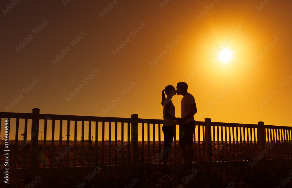Fototapeta premium Young couple kissing against a bright sunset. 