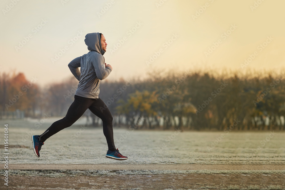 Young athletic man running at park during cold autumn morning - obrazy, fototapety, plakaty 