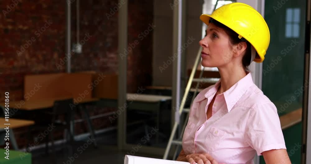 Focused architect holding blueprints and smiling at camera in the office Focused architect holding blueprints and smiling at camera in the office