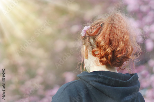 Junges Mädchen mit roten Haaren in Rückansicht schaut während der Kirschblüte in die Frühlingssonne - Young girl with red hair in rear view looks during cherry blossom in the spring sunshine