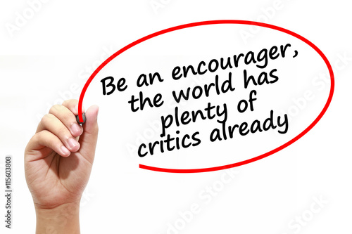 Man writing Be an encourager,the world has plenty of critics already with marker on transparent wipe board.