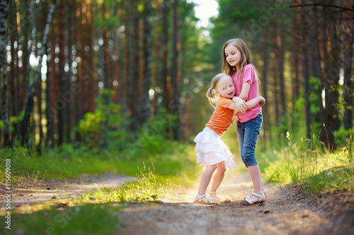 Two adorable little sisters hiking in a forest on summer