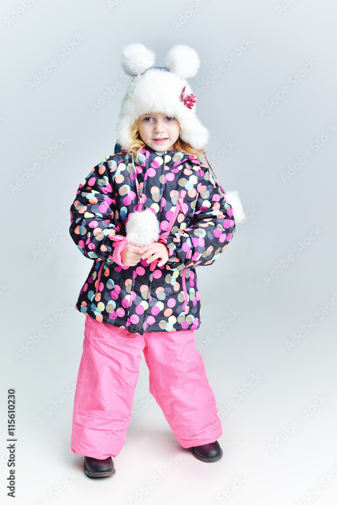 Cute little funny child in colorful winter clothes having fun with snow, outdoors during snowfall. Active outdoors leisure with children in winter. Kid with  hat, hand gloves with stripes.