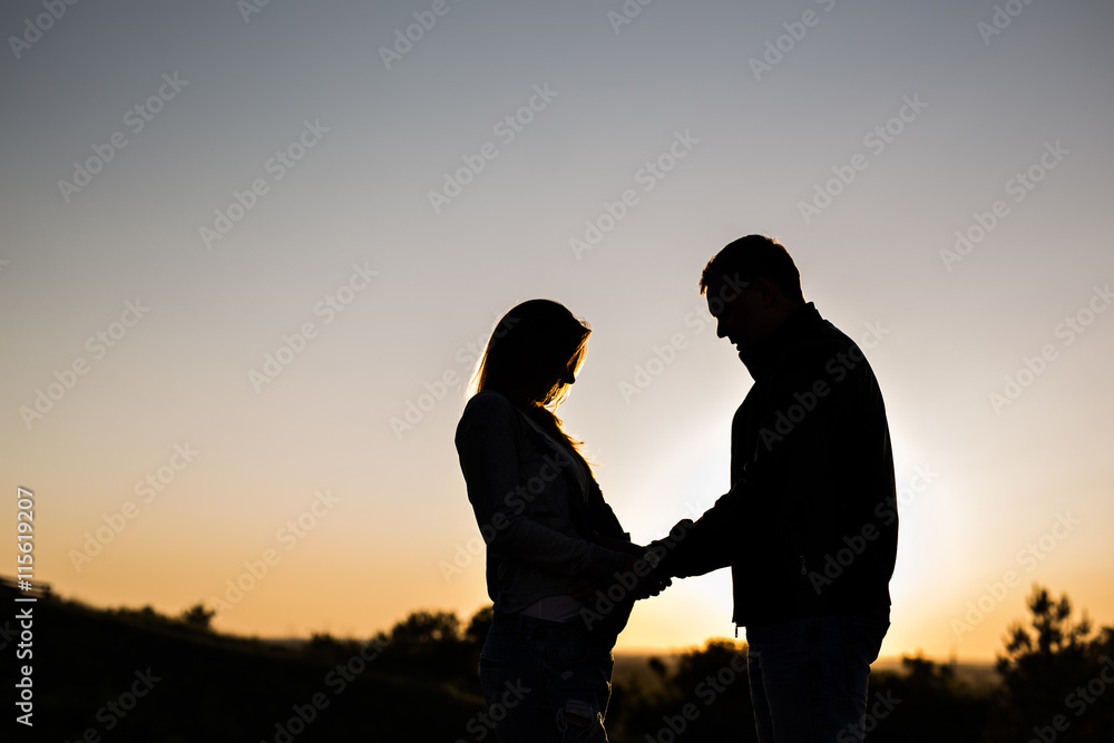 Silhouette of a pregnant woman with husband in sunset