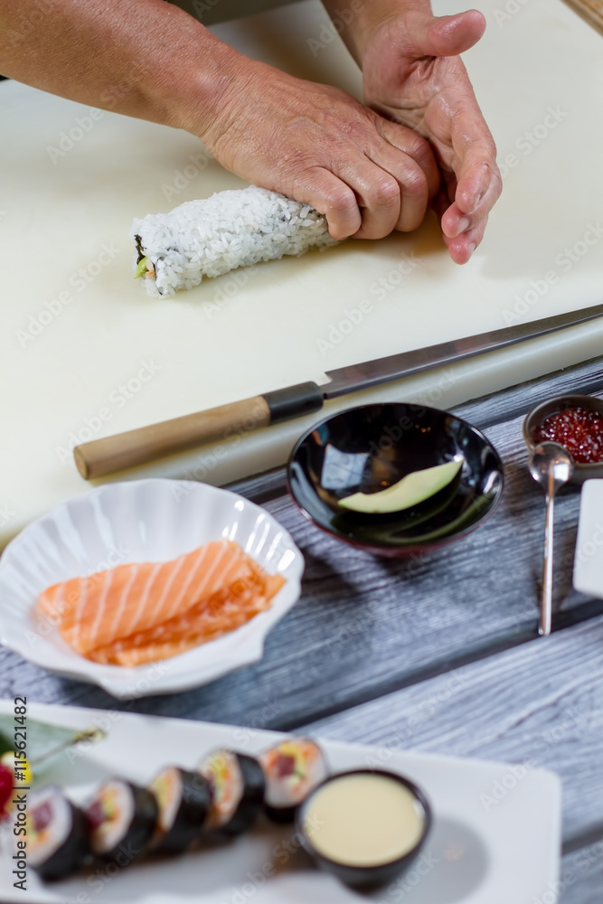 Male hands touch sushi roll. Bowl with piece of avocado. Original recipe of uramaki rolls. New dish in sushi cafe. Male hands touch sushi roll. Bowl with piece of avocado. Original recipe of uramaki rolls. New dish in sushi cafe.