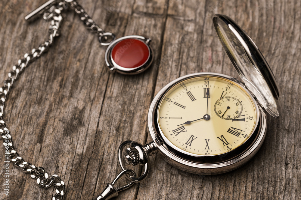 Old fashioned pocket watch with chain on rough wood 