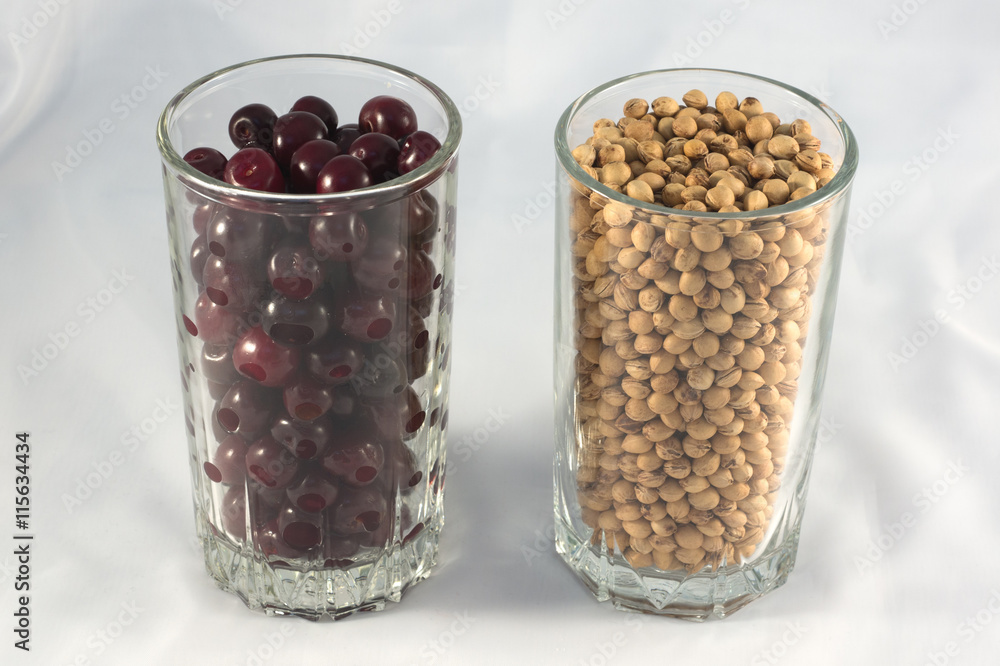 A glass of ripe cherry and a glass of cherry stones on a white background