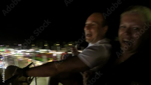 Excited couple having fun on the roller coaster ride in the amusement park at night.