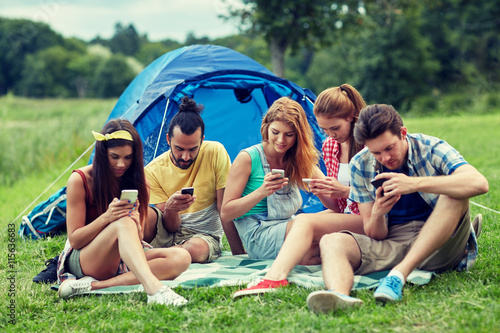 friends with smartphone and tent at camping
