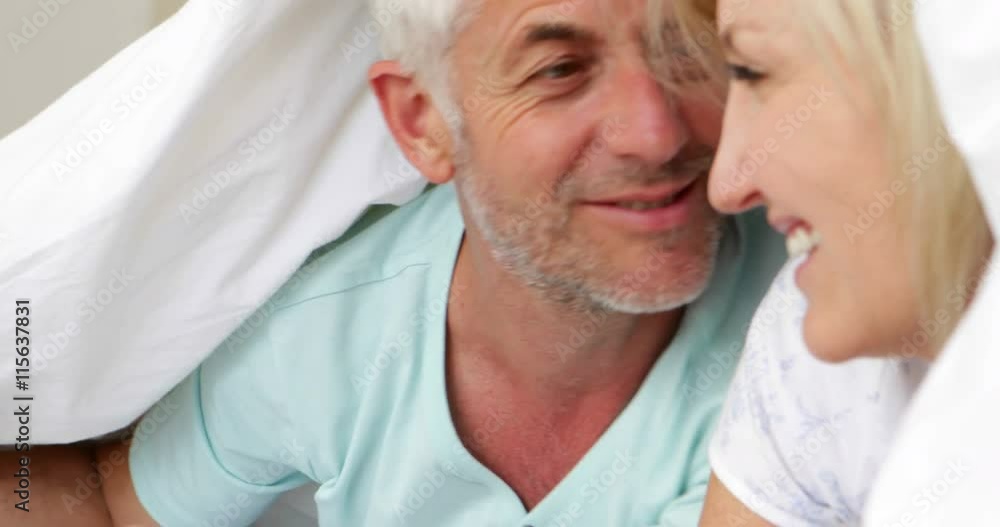 Smiling couple under the cover together in bed