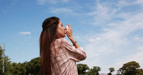 Pretty brunette using her inhaler on a sunny day