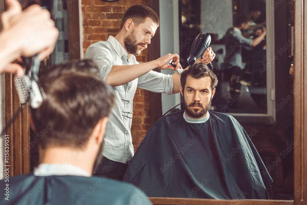 Young handsome barber making haircut of attractive man in barbershop Young handsome barber making haircut of attractive man in barbershop