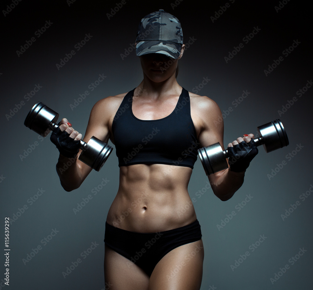 Strong fitness woman bodybuilder with tanned body pumps up the muscles lifting dumbbells.
