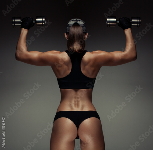 Strong fitness woman bodybuilder with tanned body pumps up the muscles lifting dumbbells. 