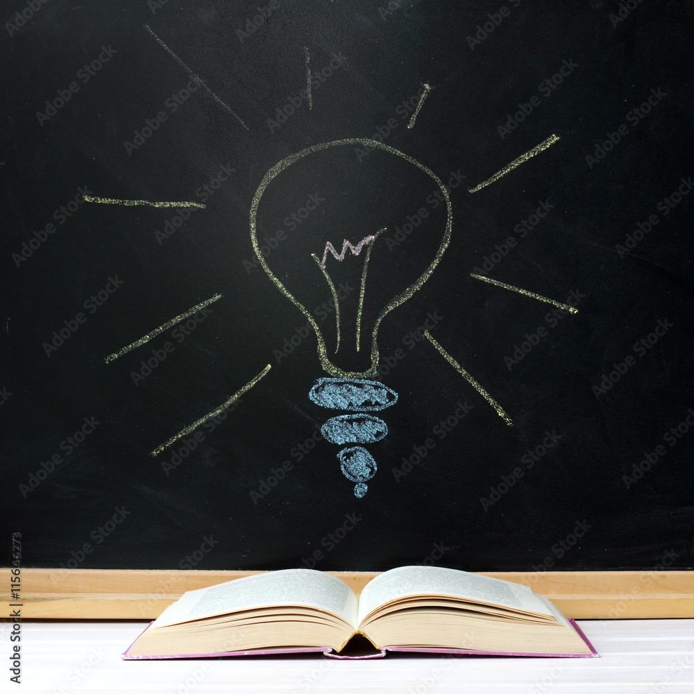Fototapeta searching for new ideas/ Opened book on background of blackboard and chalk drawn light bulb