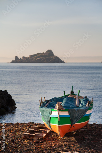 Mediterranean seascape: fishing boat near Acitrezza, Sicily, and a sea lava stack in the distance photo