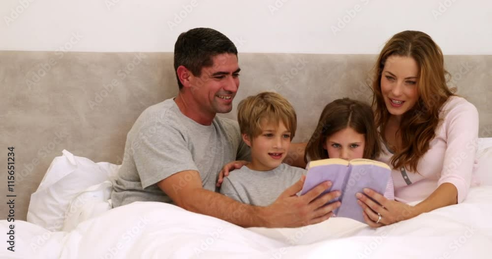 Happy parents and children reading together in bed Happy parents and children reading together in bed