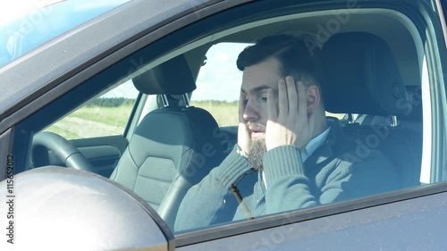 young handsome hipster man sits alone in the car in hot weather - sun is shining on him