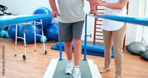 Physiotherapist helping patient walk with parallel bars