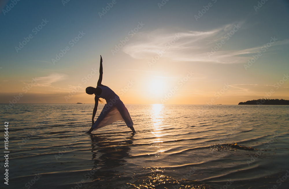 Young woman doing yoga at the beach at sunset