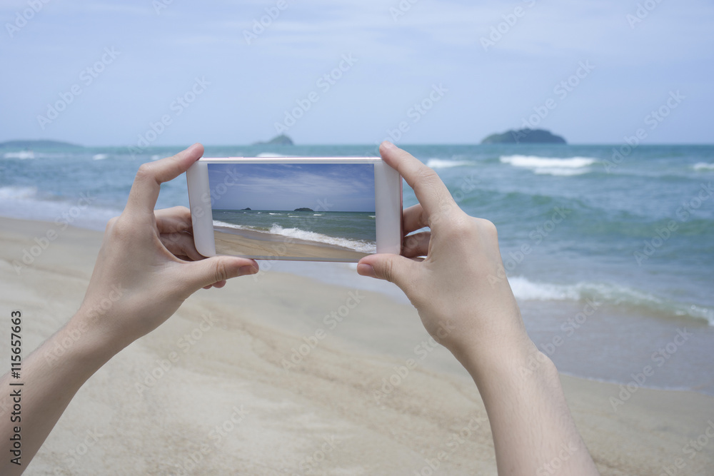 Close up of woman's hand holding smartphone, mobile, smart phone over blurred beautiful blue sea to take a photo of the sea